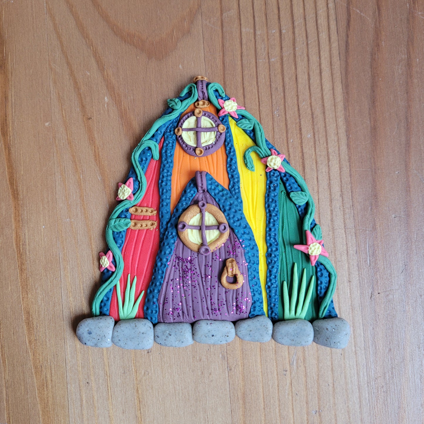 The Pride fairy door is rainbow colored and rests on a wooden background.