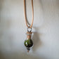 Closeup. A teardrop shaped tiny terrarium with live moss hangs on a brown necklace. By Planted Glass Terrariums in Edmonton.