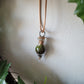 A teardrop shaped tiny terrarium with live moss hangs on a brown necklace. By Planted Glass Terrariums in Edmonton.